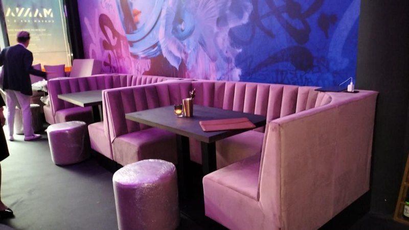 Roze fluwelen booths rond donkere tafels; achter de banken loopt het beeld met koi en tags over de hele wand door.