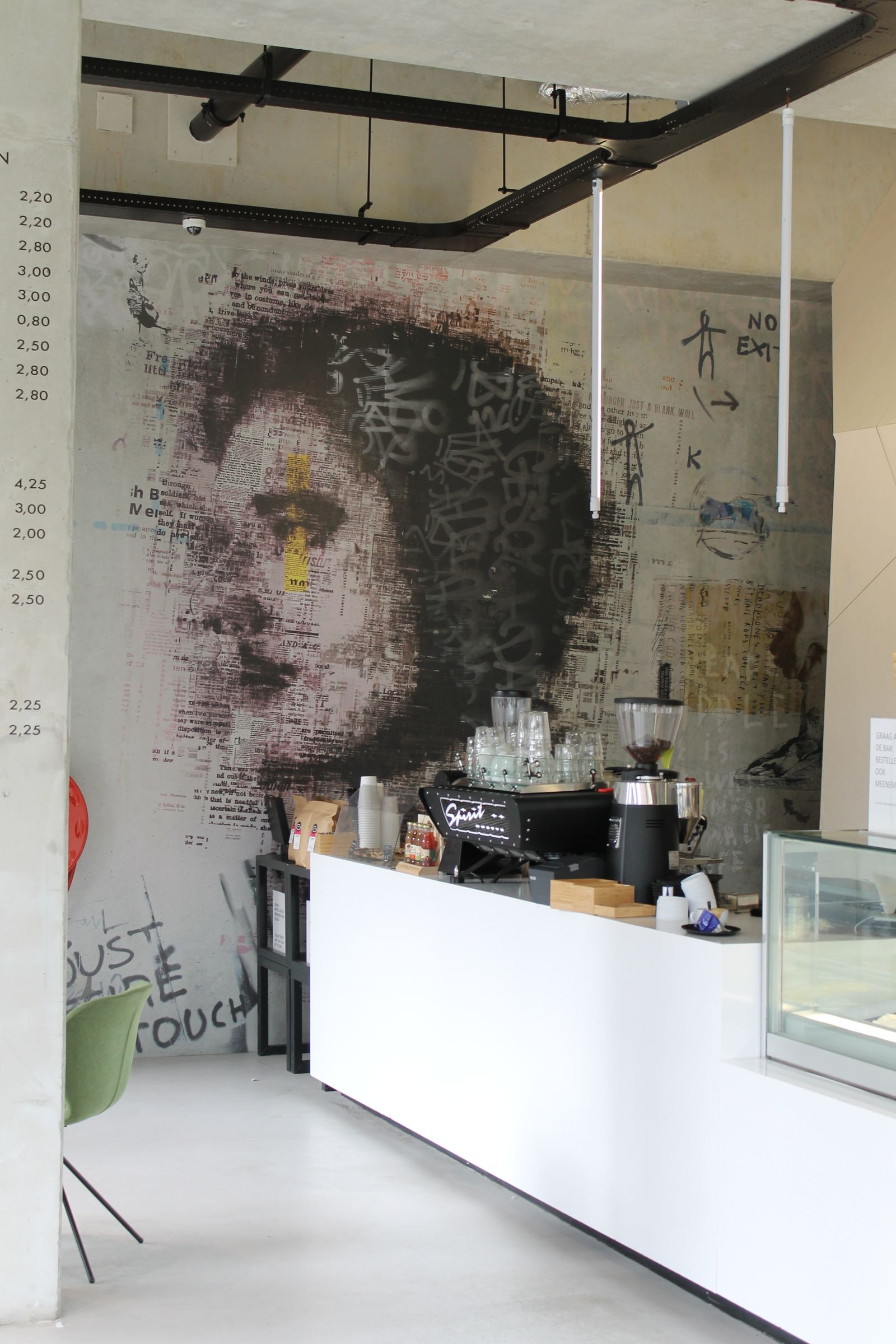Voorbeeldfoto van een cafémuur, recht van voren: een portret opgebouwd uit lagen krantendruk en zwarte kalligrafie, achter de toonbank.