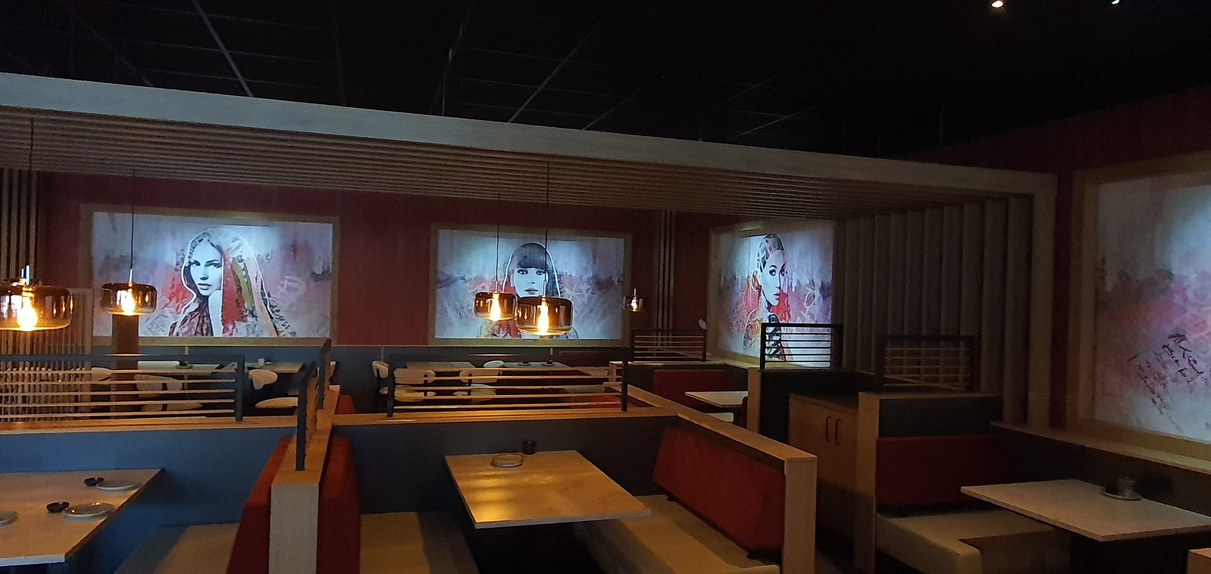 Restaurantzaal met houten lamellenwanden en drie van achteren verlichte portretpanelen boven de booths.